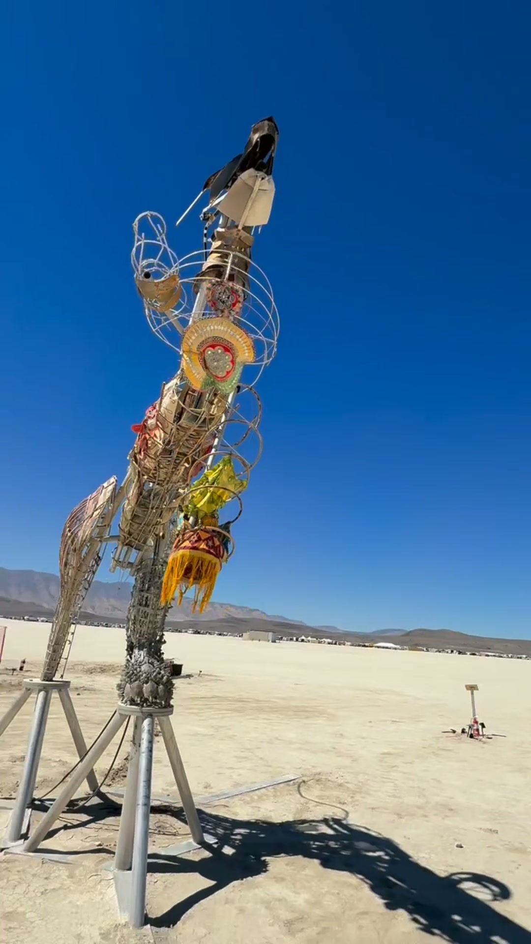 Navagunjara Reborn in daylight on the playa, 2026: woven cane leg, bronze tigress leg, raised arm, dragon's head with antenna-like horns, against a cloudless sky.