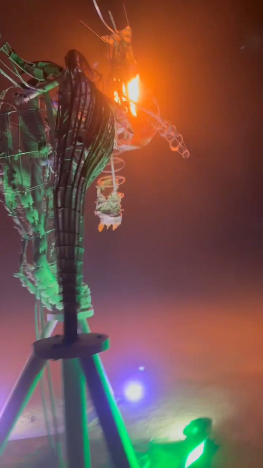 Close view at night: flame burning at the dragon's head above the woven cane body, lit green from below.